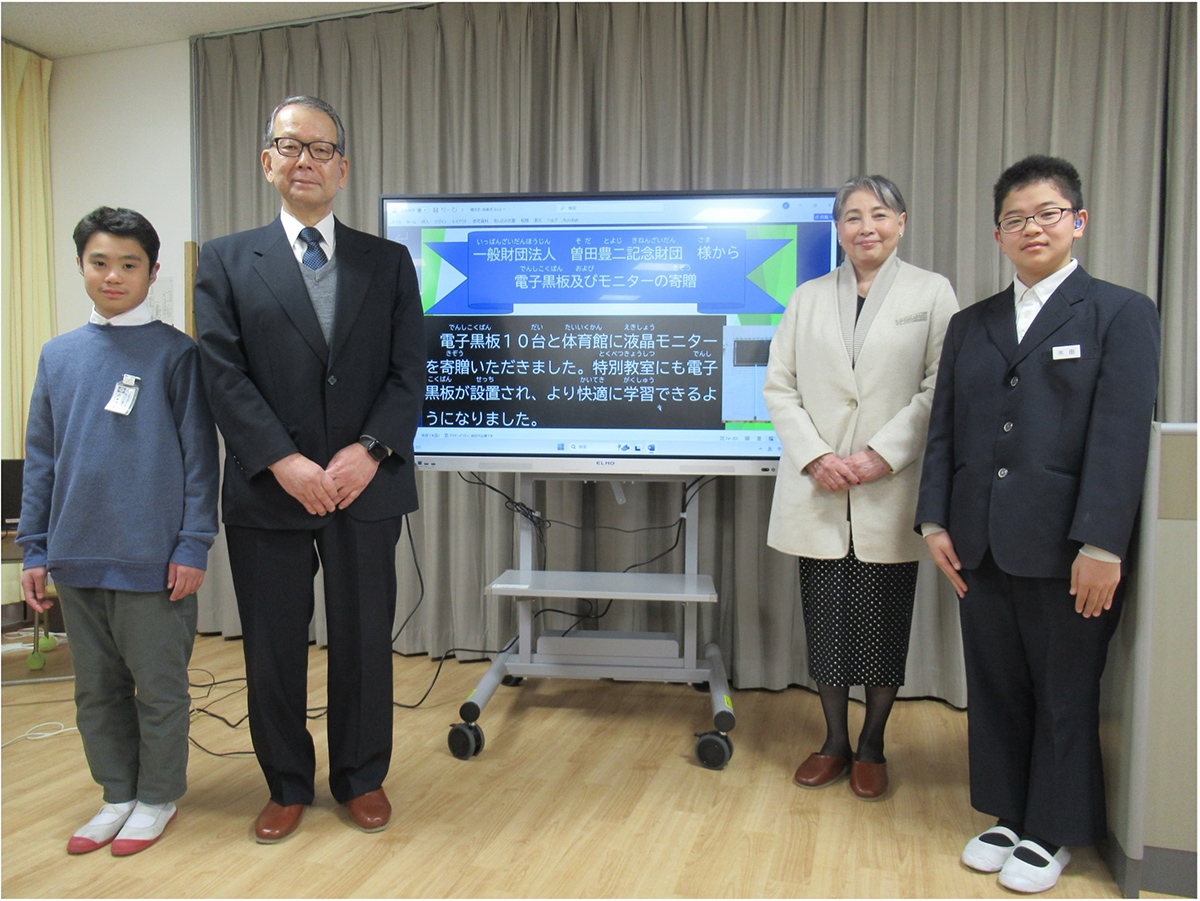 曽田豊二記念財団による電子黒板寄贈式の様子。電子黒板の前で関係者と生徒が並んでいる。